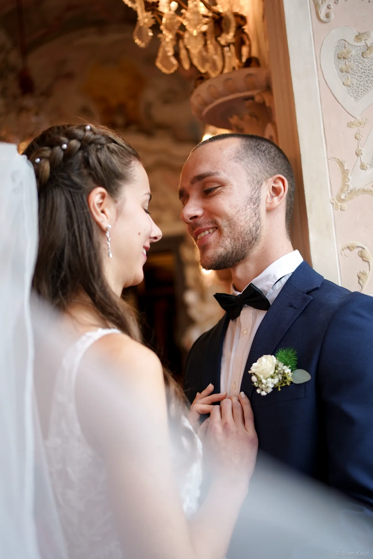 Hochzeitspaar lächelt sich in einem barocken Saal an, Braut mit Schleier